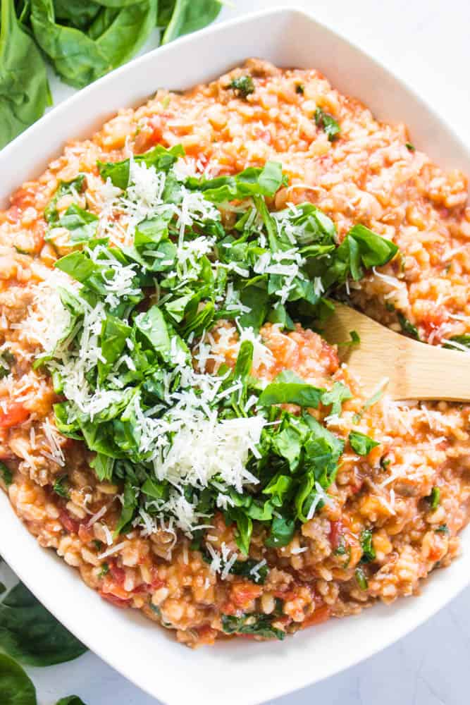 top down photo of Tomato Sausage Risotto in a square serving dish with a wooden spoon