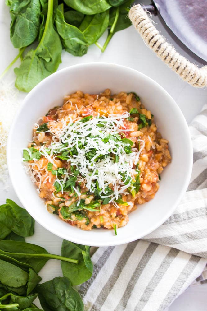 top down photo of Tomato Sausage Risotto in a white bowl garnished with basil and parmesan