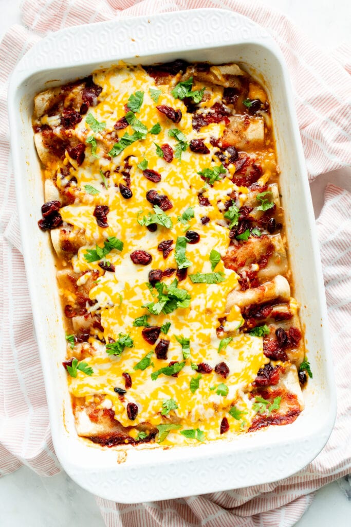 Baked enchiladas with toppings in baking dish viewed from above