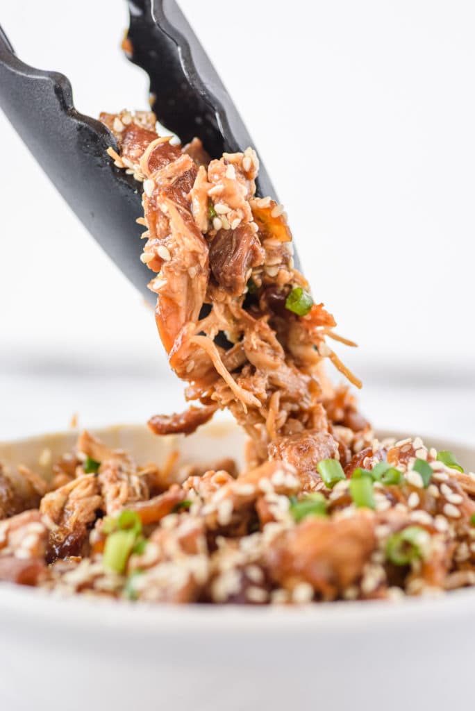 close-up photo of tongs grabbing shredded chicken