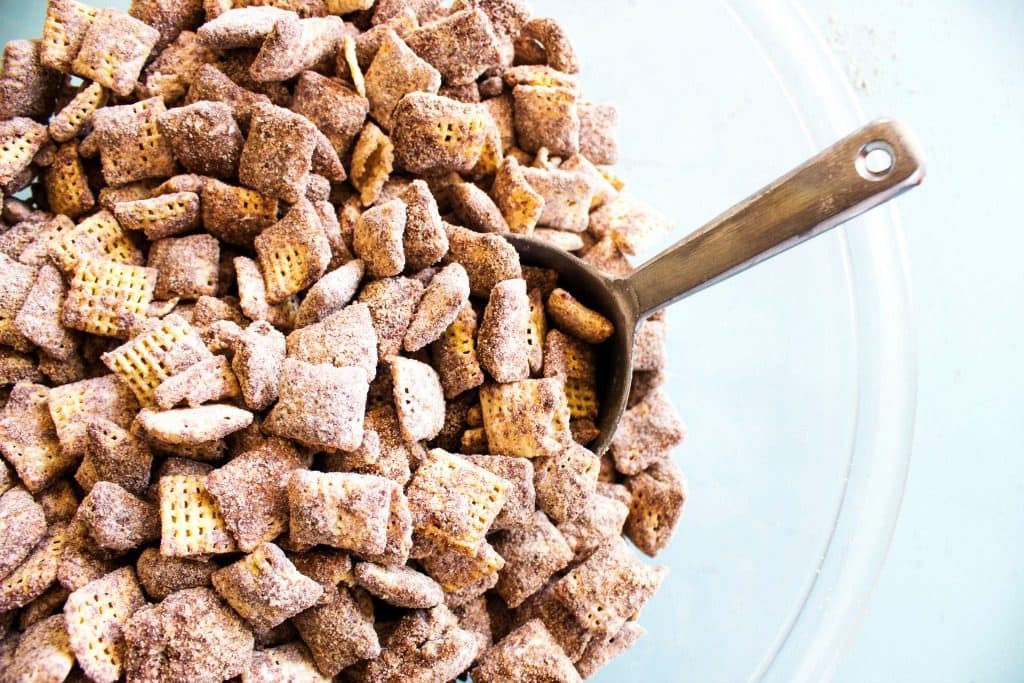 Bowl of chocolate churro muddy buddies with metal scoop