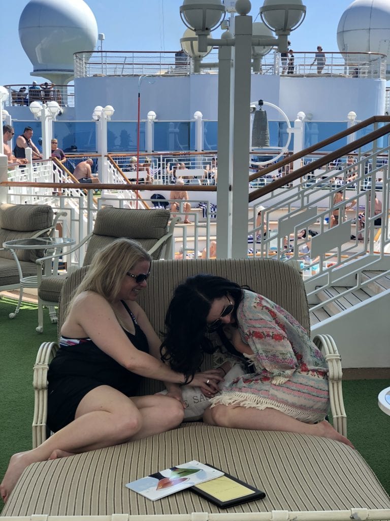 photo of 2 women laughin on a large loveseat on cruise ship deck