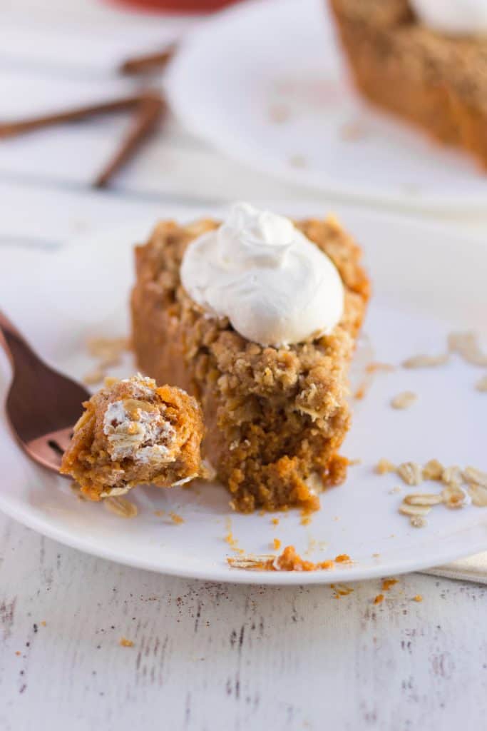 Pumpkin Crisp Pie slice on a plate, fork with bite on it. whipped cream on top