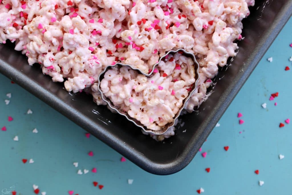 Valentine’s Day Rice Krispies Treats in a metal baking pan with a heart shaped cutter in corner of treat