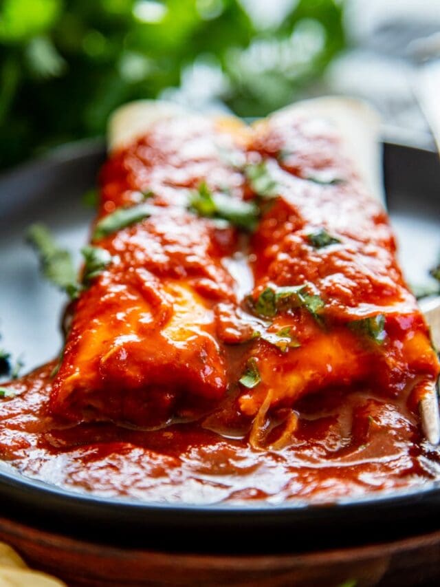 black plate with 2 cheese enchiladas with red sauce