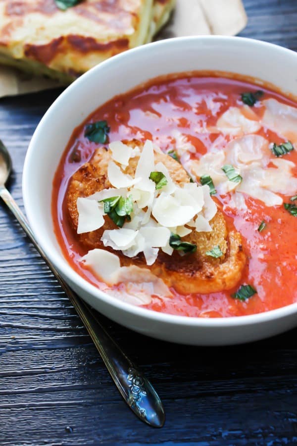 tomato soup topped with cheese and toasted bread served in a white bowl