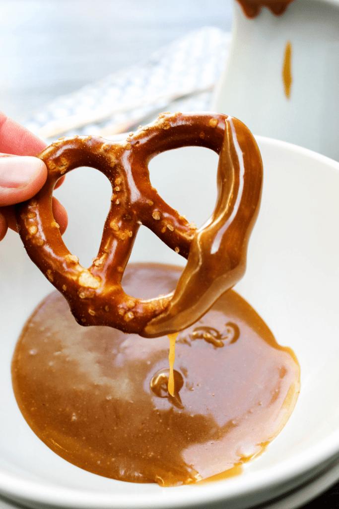 hard pretzel being dipped into a bowl of Peanut Butter Caramel Sauce