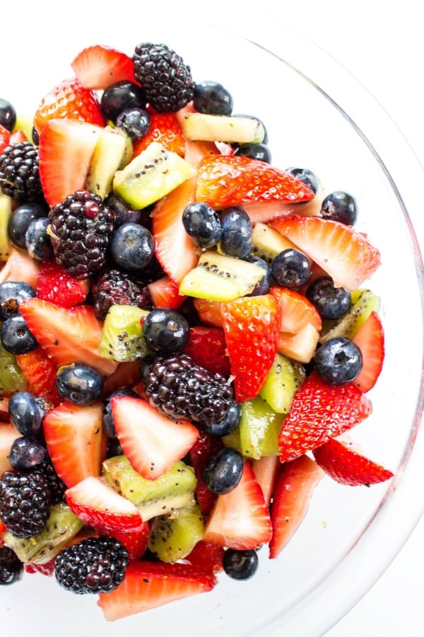 lemon poppy seed fruit salad with blackberries, strawberries, blueberries, kiwi and lemon glaze in a glass bowl