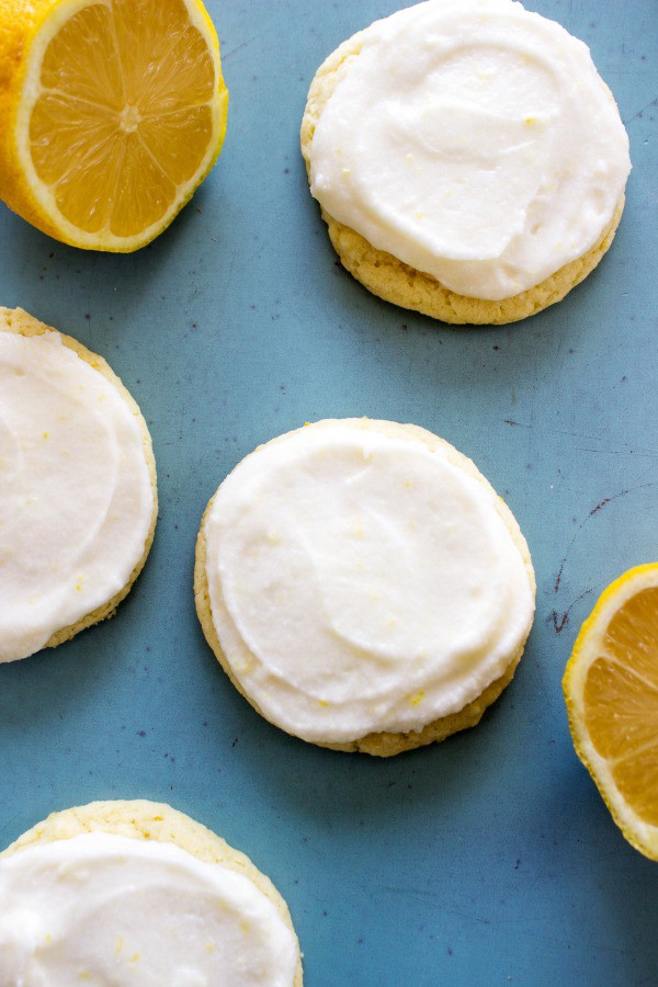 LEMON SUGAR COOKIES frosted, laid out on a counter with cut lemons