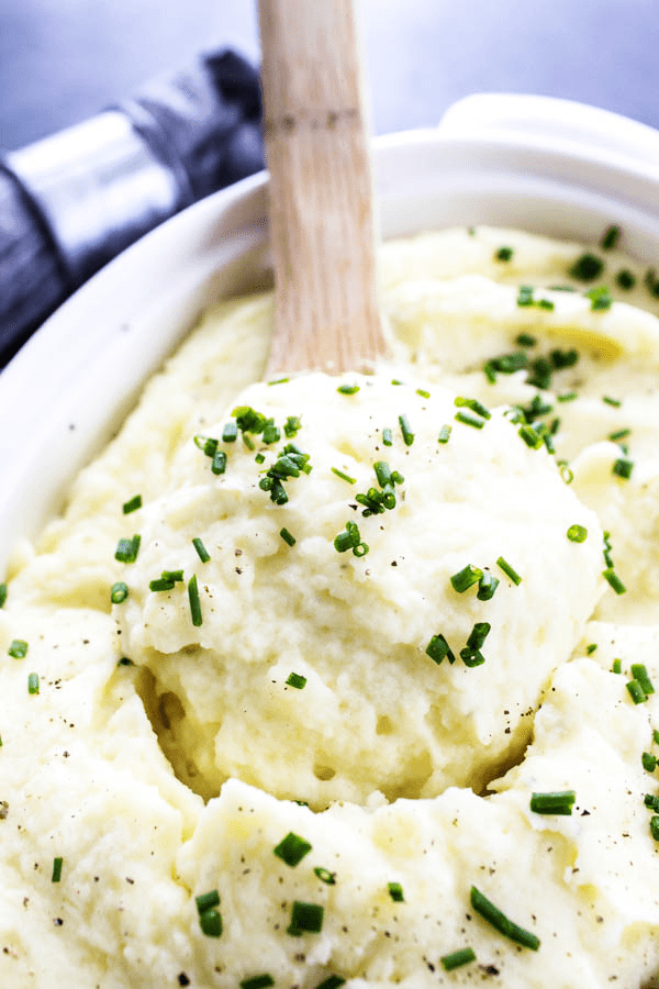 mashed potatoes topped with green onion in white serving dish with wooden spoon.