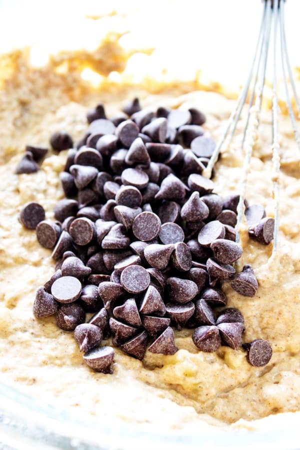 Chocolate chips being whisked into Banana Chocolate Chip Muffin batter in a glass bowl