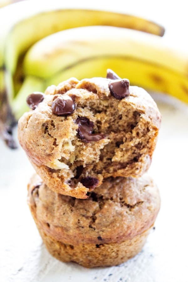 stack of Banana Chocolate Chip Muffins with a bite taken out of the top one, bananas in background