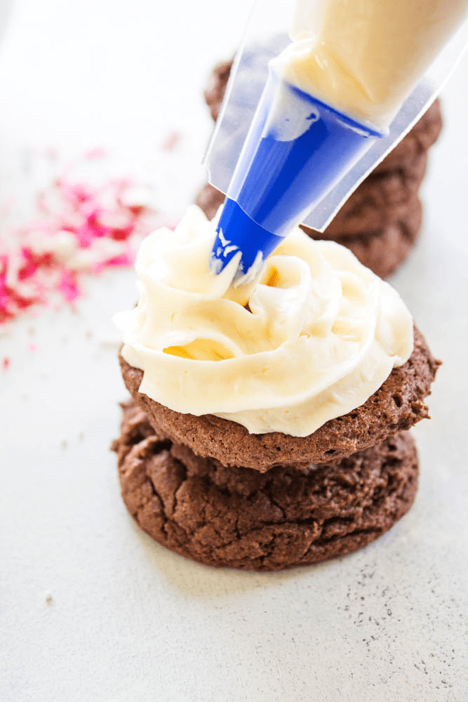 piping bag piping cream cheese frosting onto a chocolate cake cookie