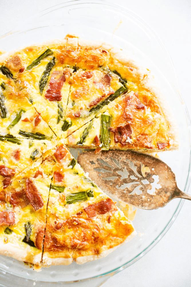 overhead photo of a sliced quiche in a glass pie pan with a slice removed