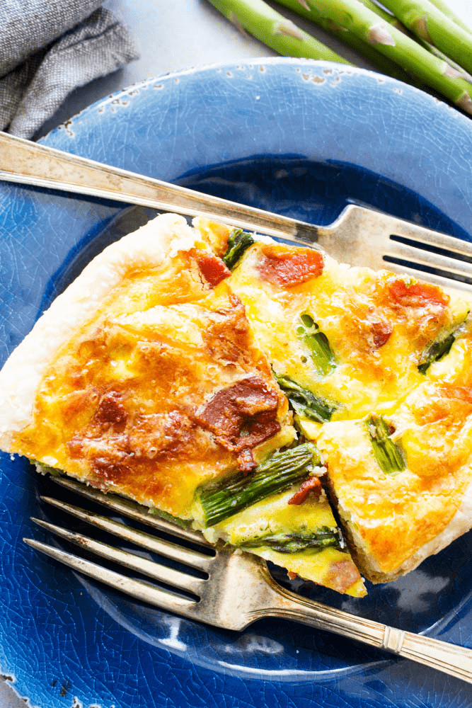 2 slices of asparagus bacon quiche on a blue plate with forks.