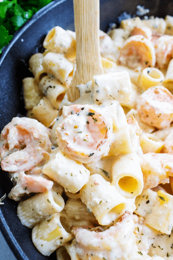 shrimp alfredo on pasta in a black bowl with a wooden spoon
