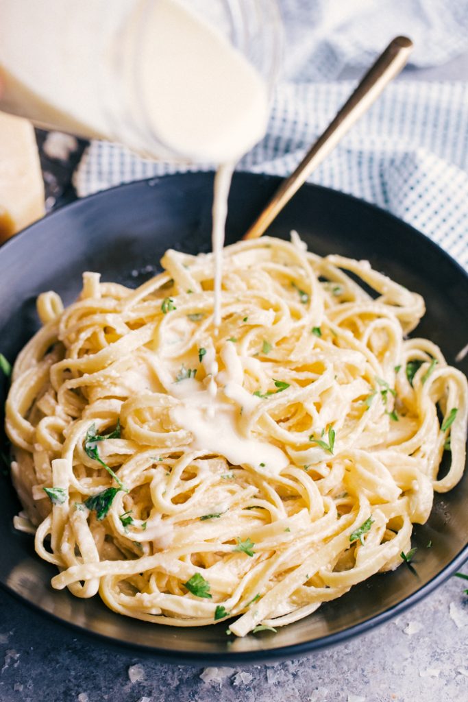 Pouring Alfredo Sauce over Fettuccine Alfredo on a black plate