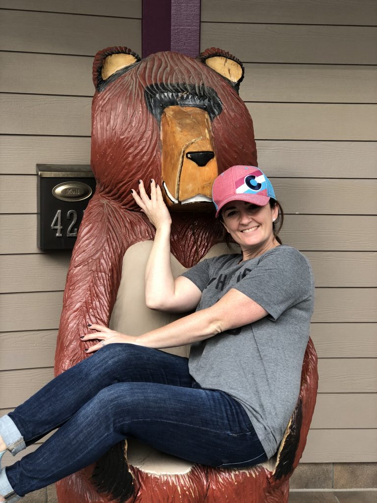 sandra sitting on lap of a wooden bear statue