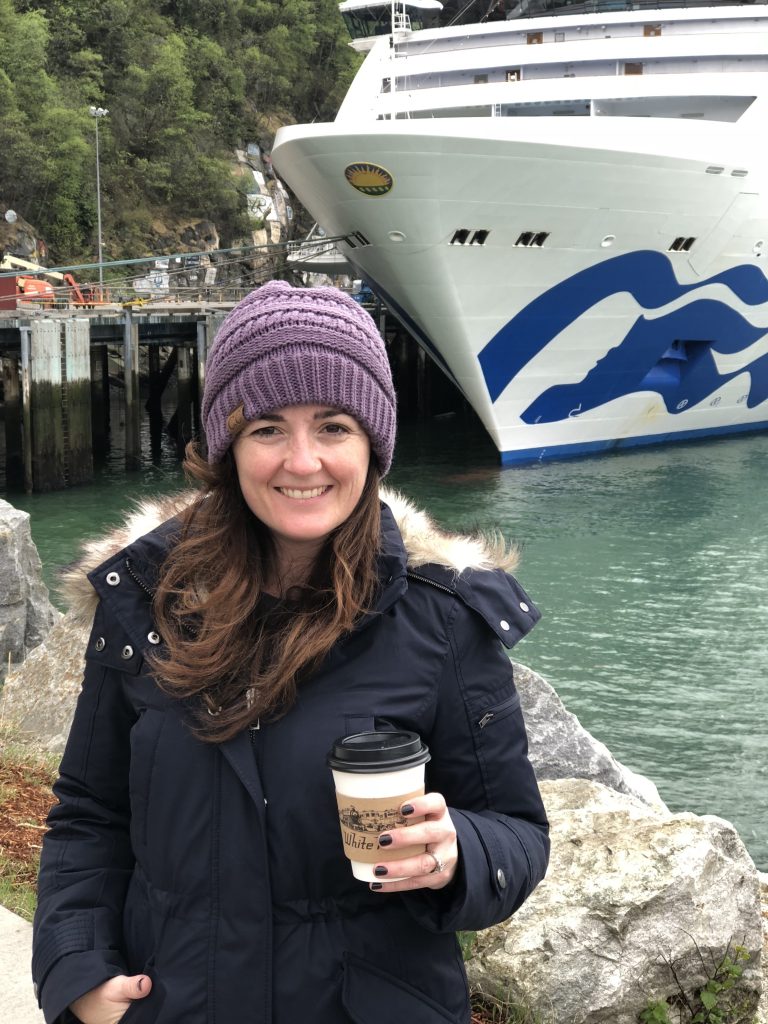 sandra in front of cruise ship holding a cup of coffee