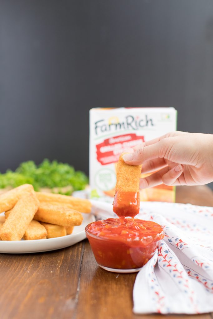 dipping a grilled cheese stick in tomato sauce in a bowl with a plate of grilled cheese sticks