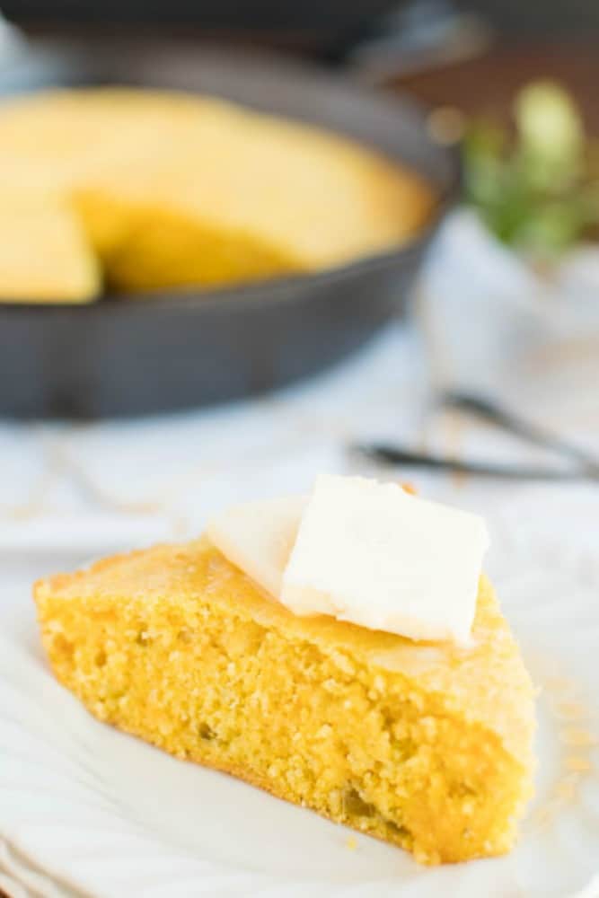 cornbread slice on a plate with butter on top. skillet in background