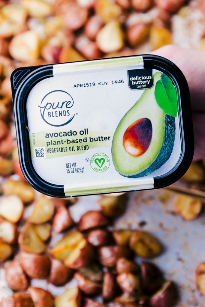 up close tub of pure blends avocado oil plant-based butter, with roasted potatoes on a sheet pan in background