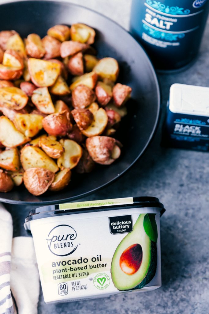 roasted potatoes in a black bowl with avocado oil butter tub on counter, with salt and pepper containers