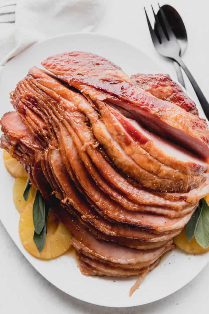 photo of sliced ham on a plate garnished with sage and pineapple rings. 