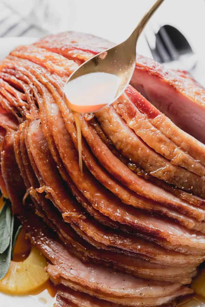 a spoonful of glaze being drizzled over the cooked sliced ham