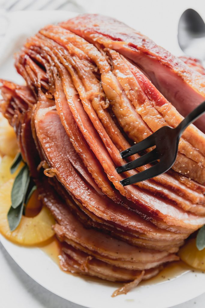 photo of sliced crockpot ham with a fork in a few slices on a serving plate with pineapple slices 