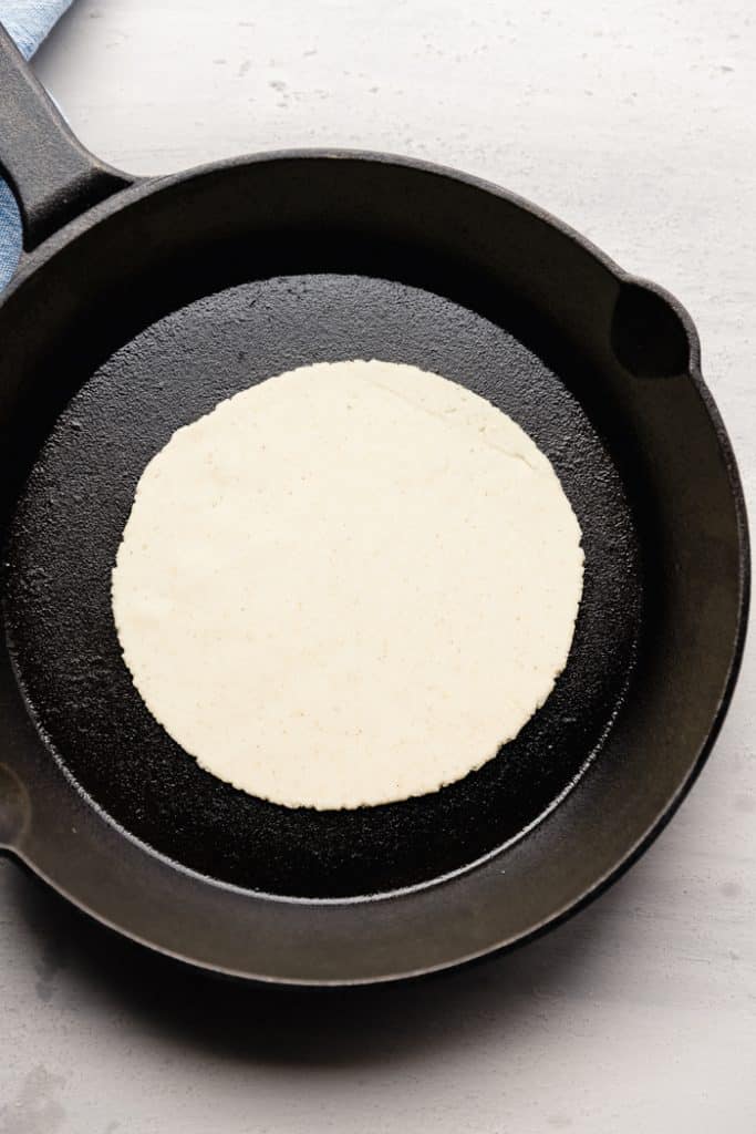 overhead photo of a raw corn tortilla in a cast iron skillet on the counter
