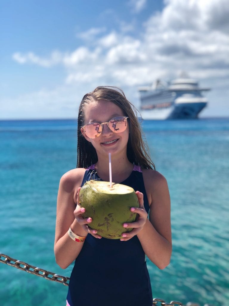 photo of teenage girl with a coconut with a straw in it, with ocean and cruise ship in the background