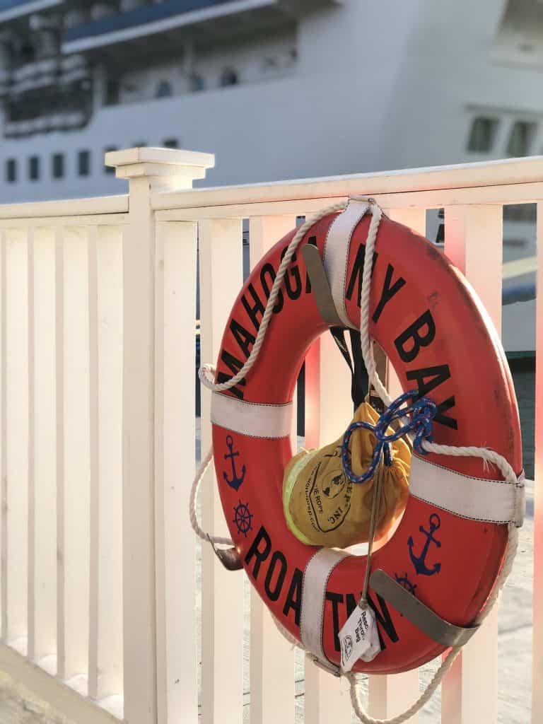 photo of a lifebuoy that says "mahogany bay" hanging on a white fence by cruise ship