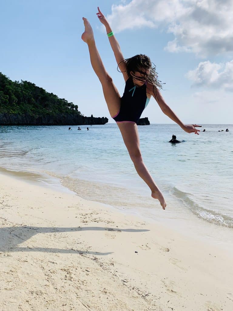 photo of teenage girl doing a vertical split leap on the beach