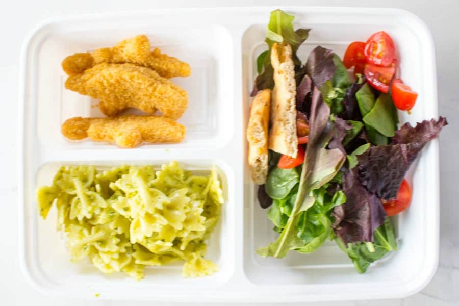 photo of lunch box with nuggets, bowtie pasta with pesto, and mixed salad greens with pita and tomato pieces