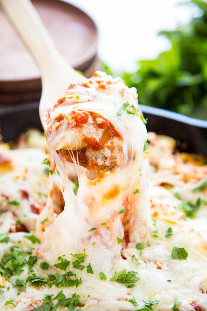 a spoon lifting a cheese stuffed pasta shell from the pan.