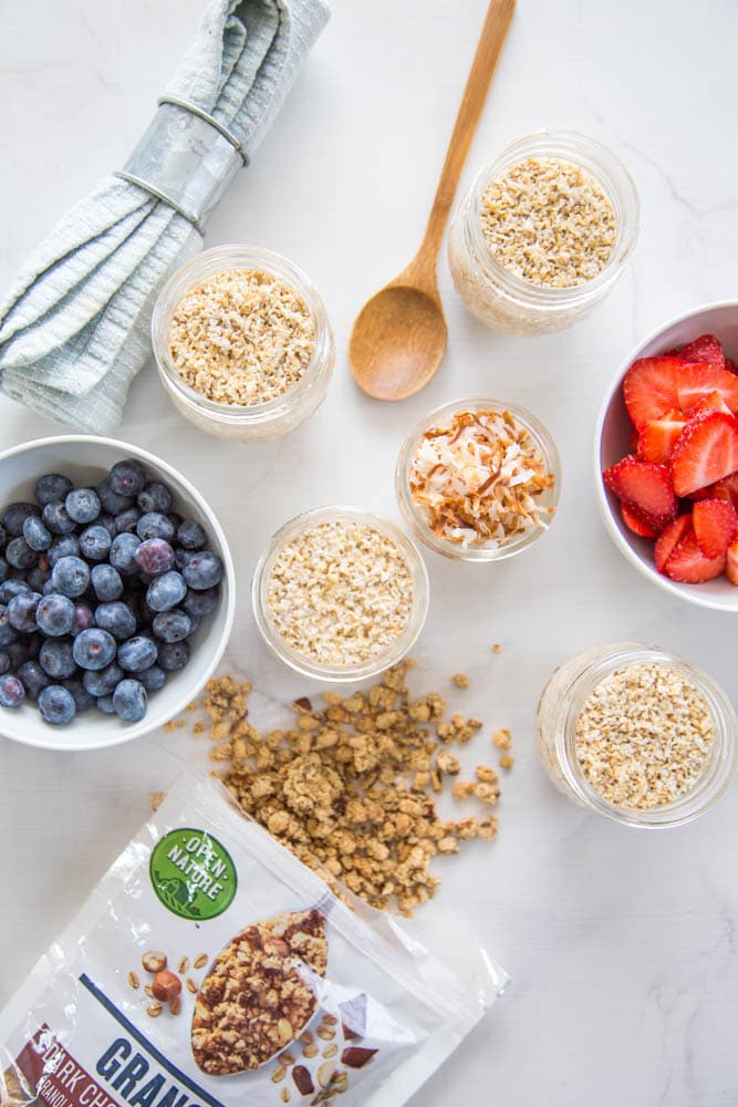 photo of overnight oats being assembled with fresh blueberries, strawberries, and other toppings