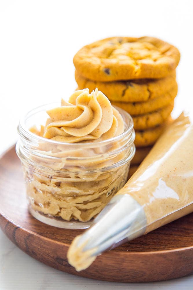 photo of a jar of frosting with a piping bag and cookies in the background.