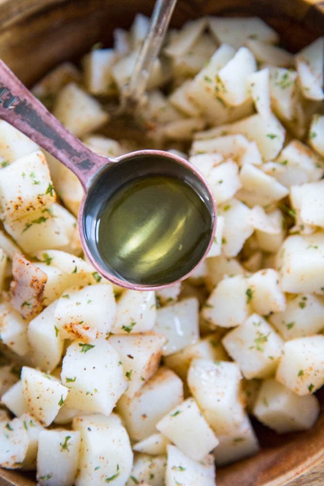 a measuring spoon of oil being poured over the potatoes