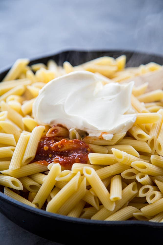 mascarpone cheese and chili paste being added to the pan.