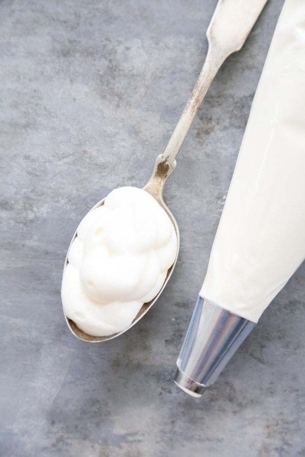 a spoonful of icing with a piping bag of icing next to it.