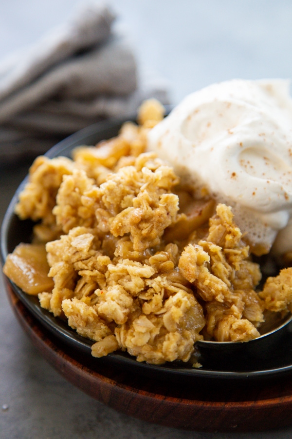 close-up shot of an apple crisp on  a plate with whipped cream.