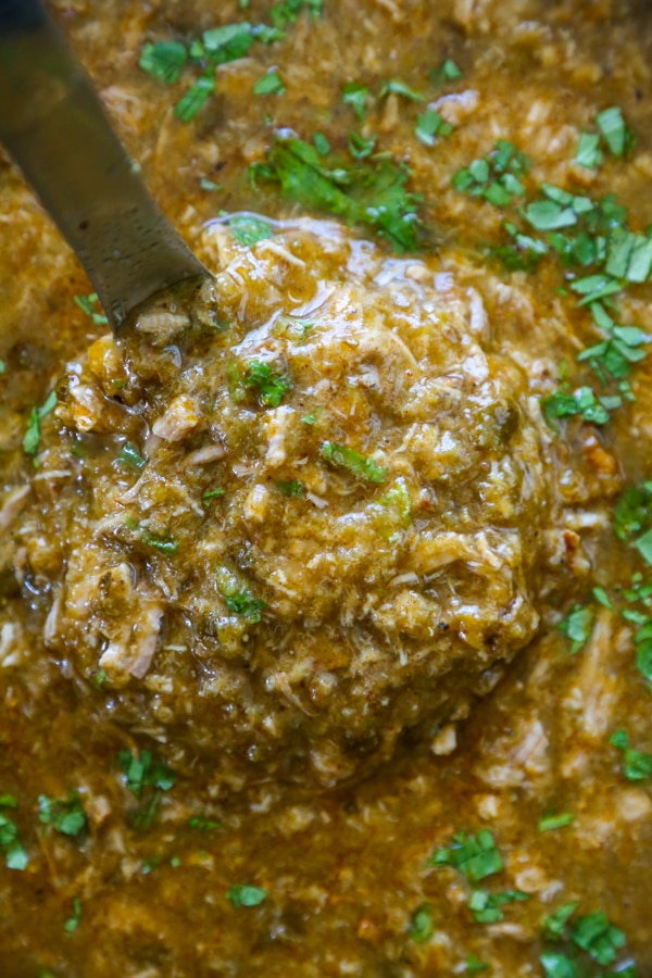 a ladle of chile verde being lifted out of a slow cooker.