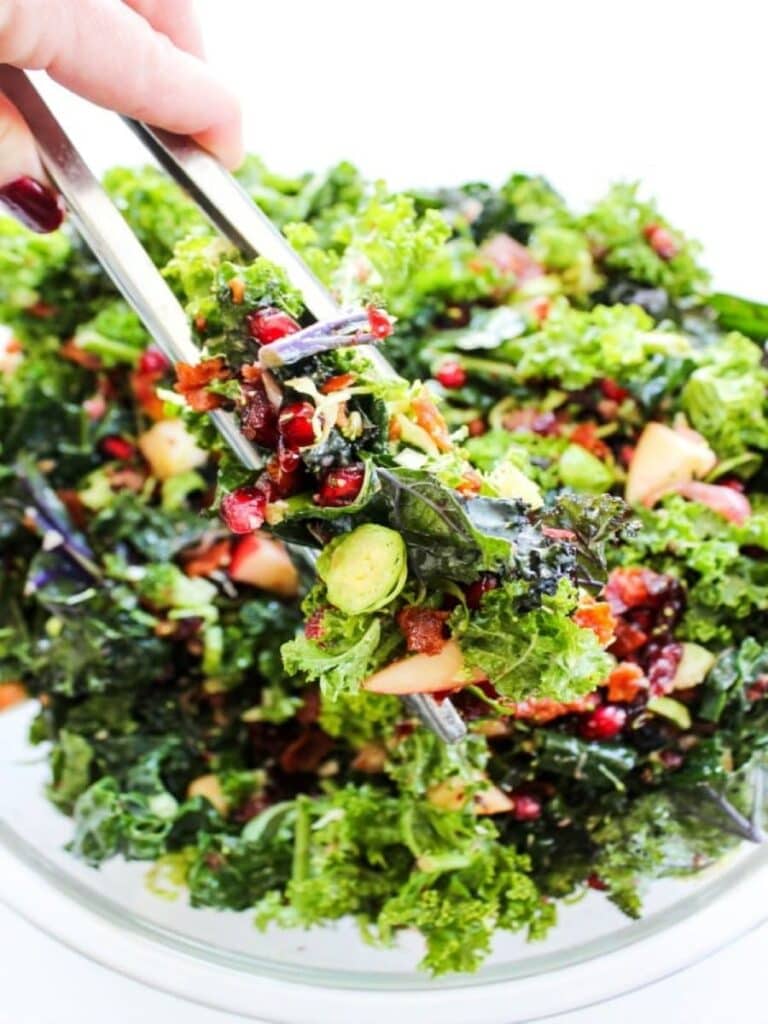 kale salad with tongs on glass bowl