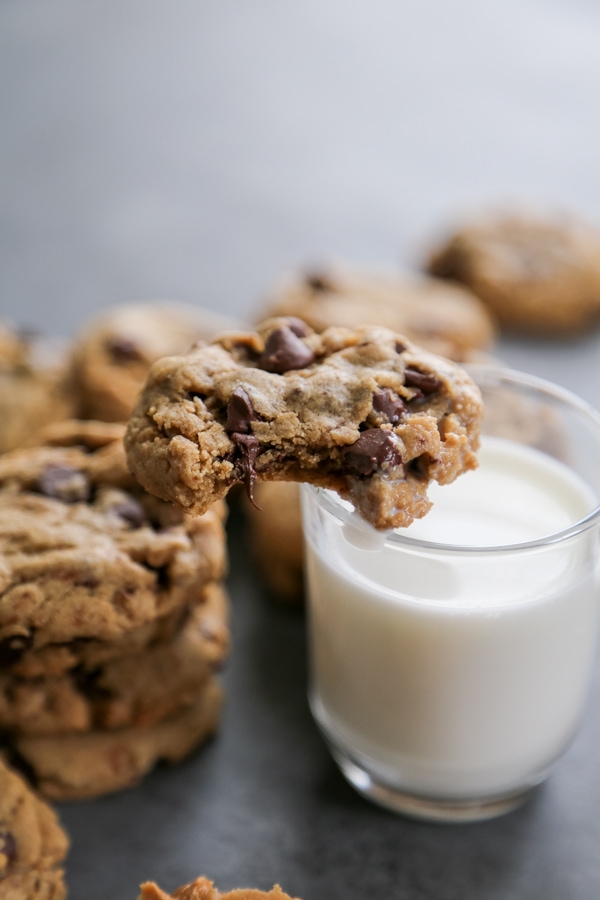 a cookie on the rim of a glass of milk with more cookies in the background.