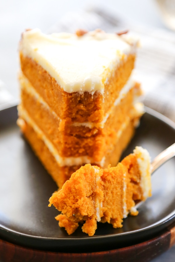 close up of a fork with a bite of cake with the rest of the slice behind it.