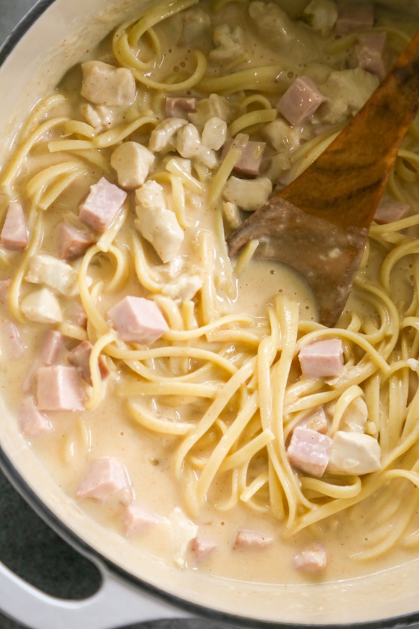 the sauce, ham, chicken, and pasta being stirred in a pot.