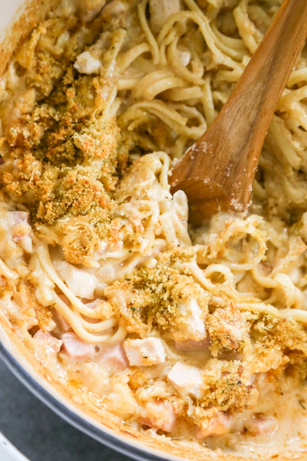 chicken cordon bleu pasta bake in a dish with a wooden spoon.