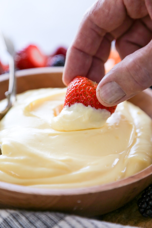 a strawberry being dipped into fruit dip.