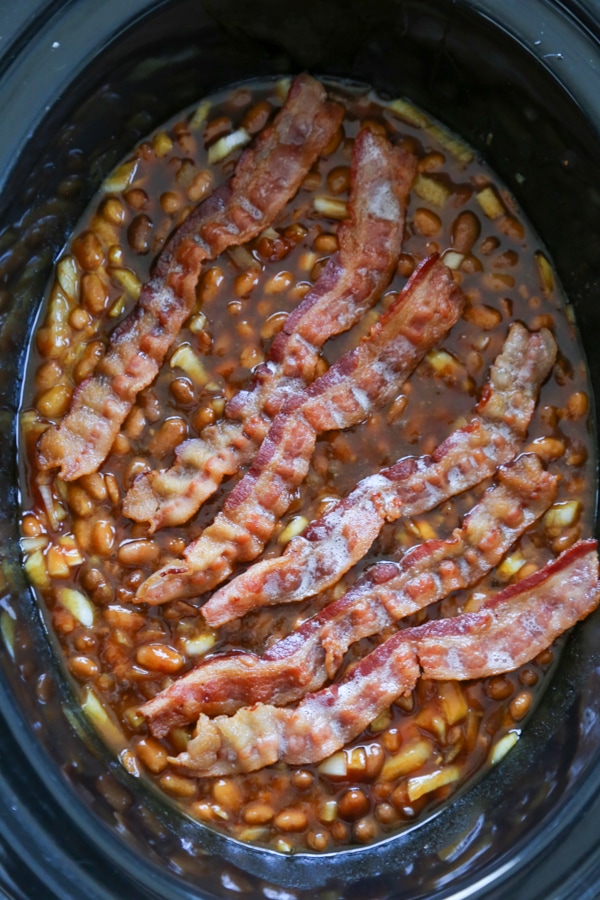 overhead shot of the baked beans in the slow cooker topped with bacon.